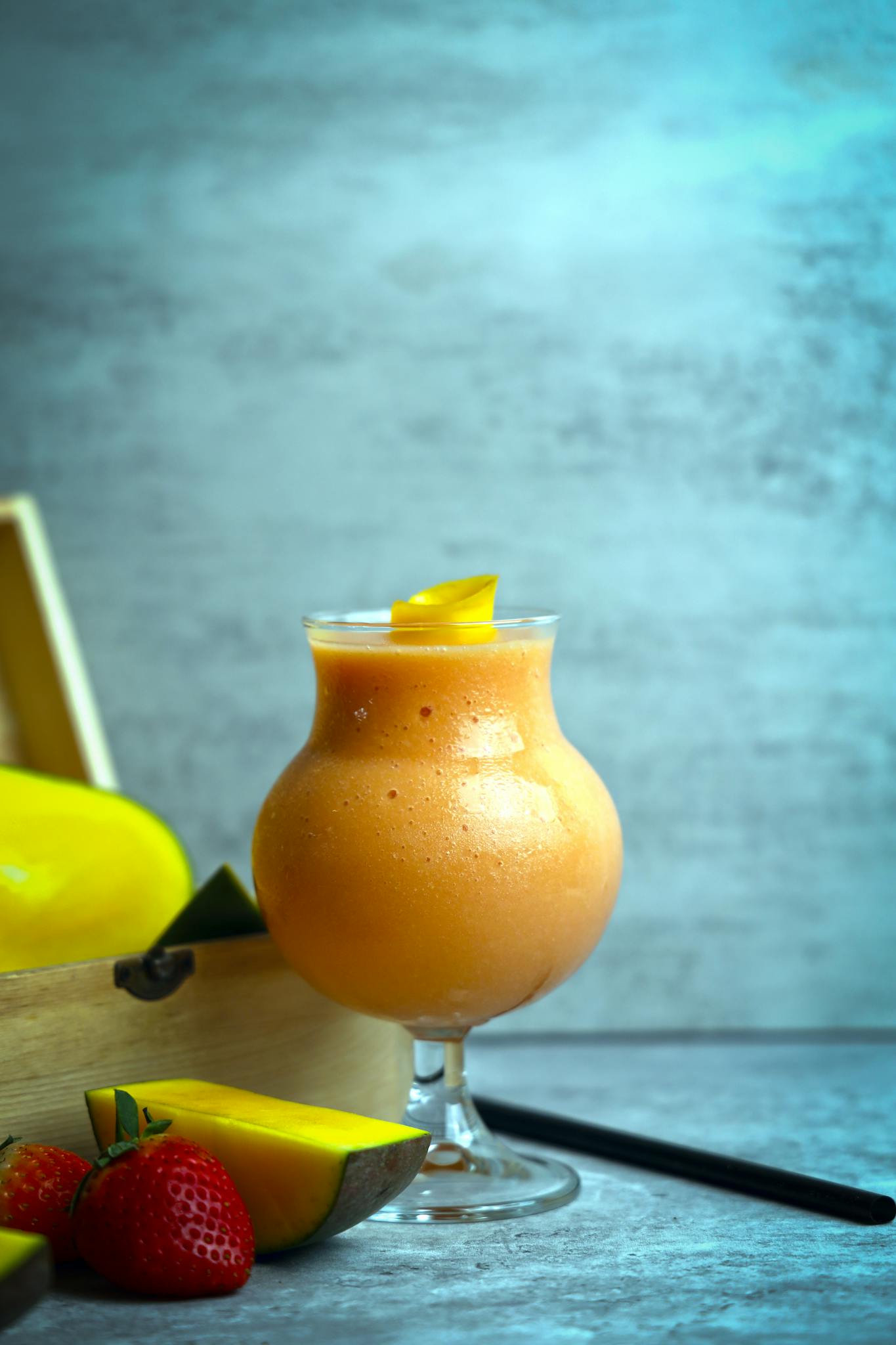 Delicious and healthy mango smoothie served in a glass with strawberries.