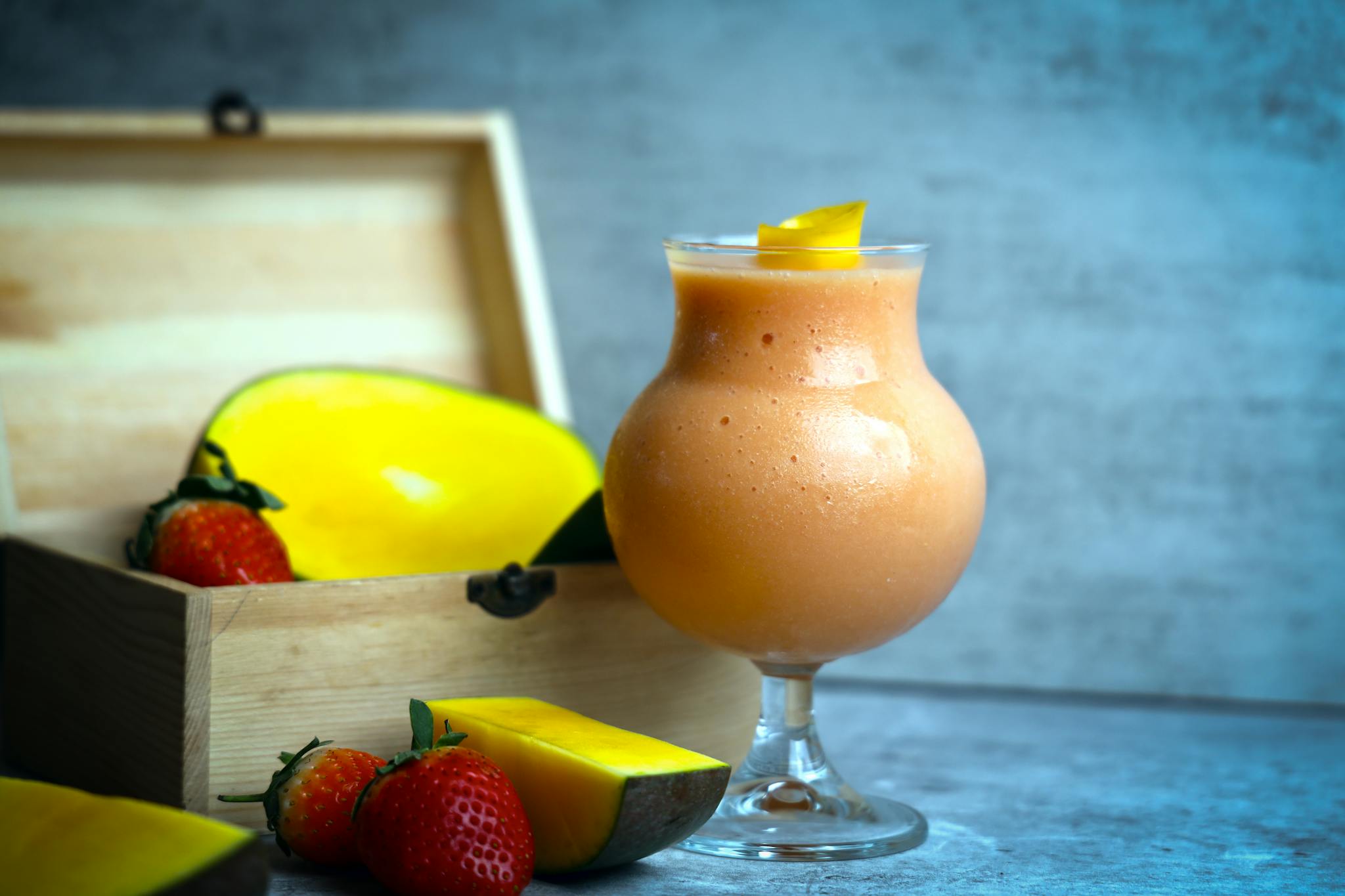 Delicious mango and strawberry smoothie served in a glass with fresh fruit beside it.