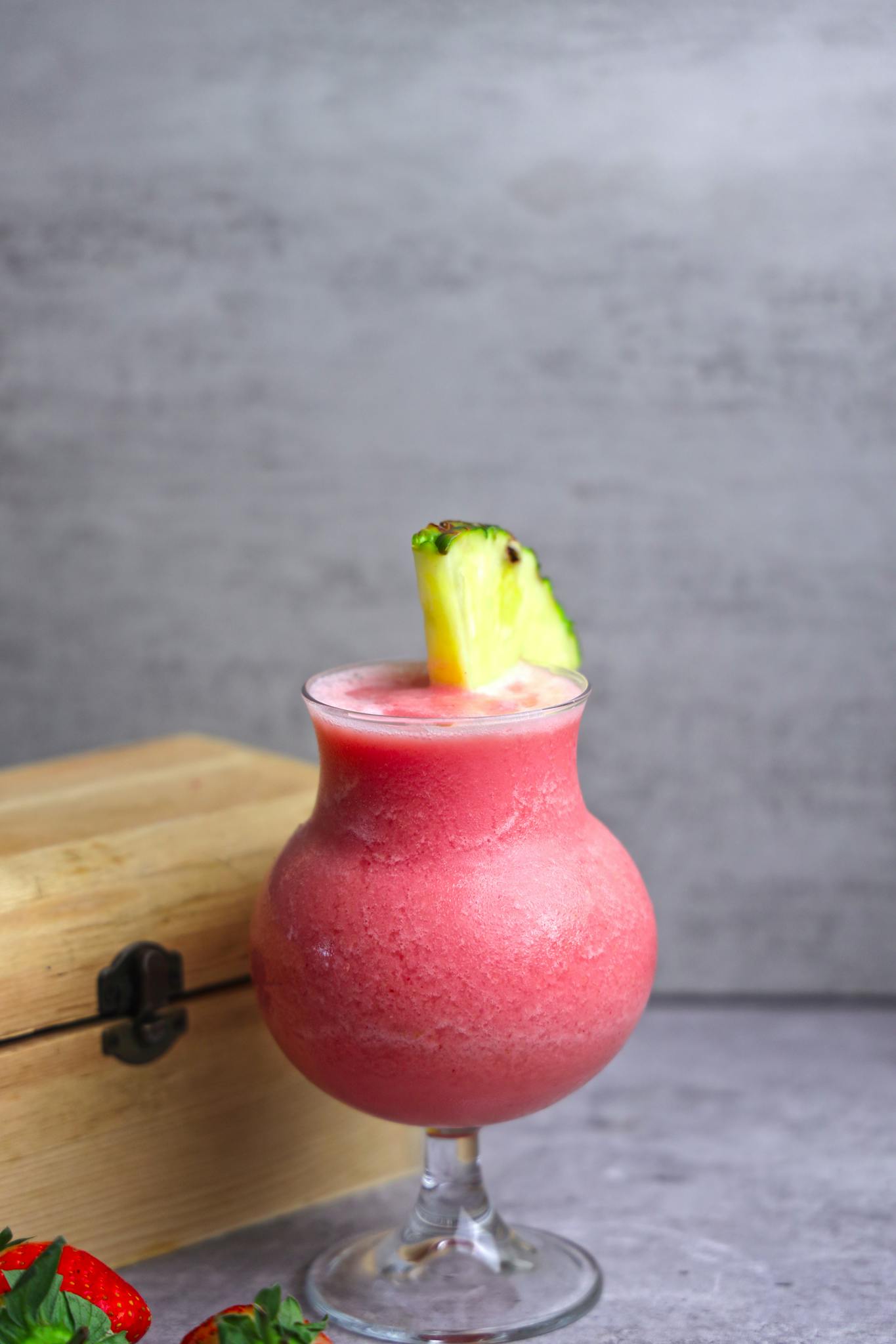 Delicious pink smoothie in a glass with a pineapple garnish on a wooden table.