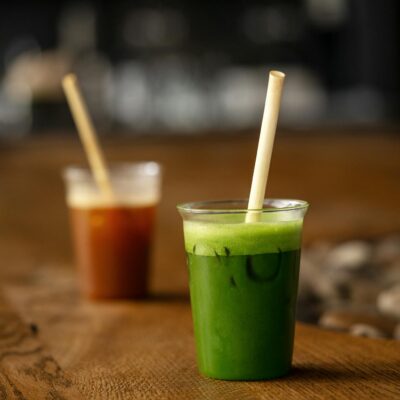 Two vibrant green and red beverages in plastic cups with bamboo straws on a rustic wooden table.