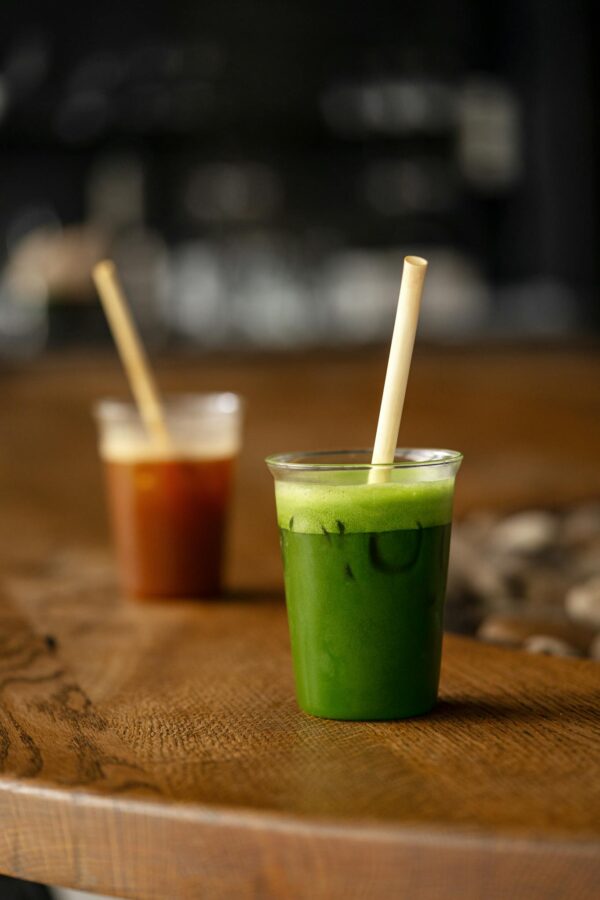 Two vibrant green and red beverages in plastic cups with bamboo straws on a rustic wooden table.