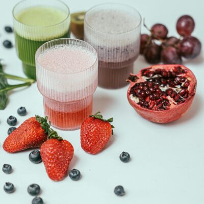Vibrant fruit smoothies surrounded by fresh strawberries, blueberries, and pomegranate on a white background.