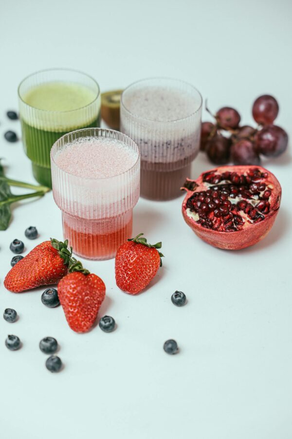 Vibrant fruit smoothies surrounded by fresh strawberries, blueberries, and pomegranate on a white background.